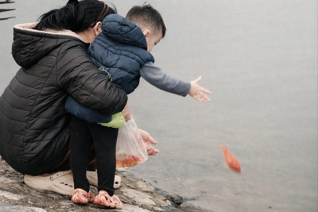 Người lớn hướng dẫn trẻ em cách thả cá trong ngày lễ âtos quân. Ảnh: Hoàng Hiền.